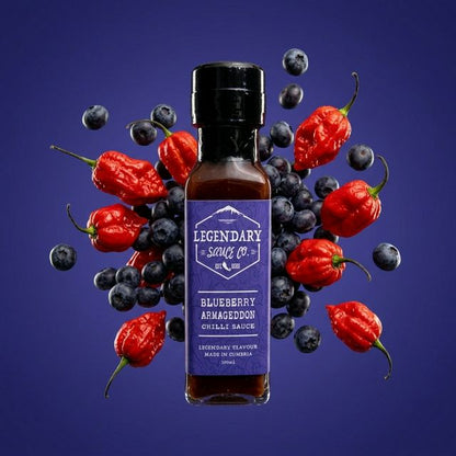 Bottle of Legendary Sauces Co. Blueberry Armageddon Chilli Sauce surrounded by blueberries and red chilli peppers on a purple background.