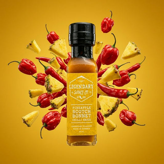 Bottle of Legendary Sauces Co. Pineapple Scotch Bonnet Chilli Sauce with peppers and pineapple on a yellow background